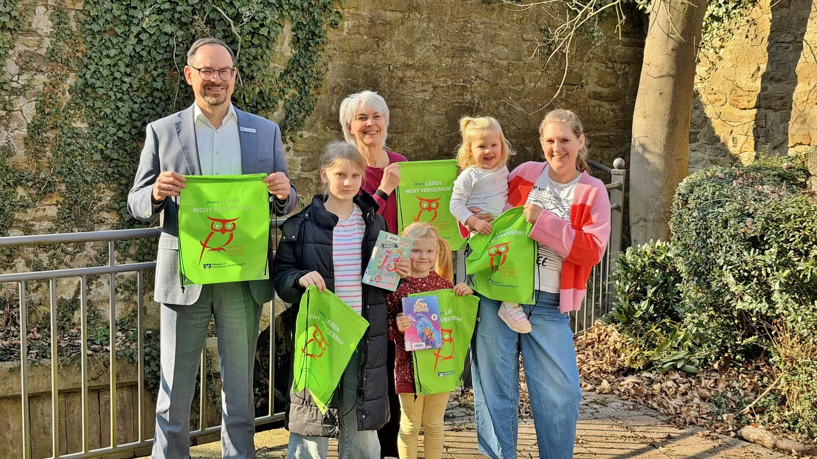 Mama Johanna weiß, dass Moira, Geesje und Leevke wahre Leseratten sind und holt sich zusammen mit ihren Kindern die grünen Lesebeutel in der Stadtbücherei ab, die von Manuel Wiegand von der Volksbank in Schaumburg und Nienburg eG an Büchereileiterin Bärbel Hanauske übergeben wurden. (Foto: ste)
