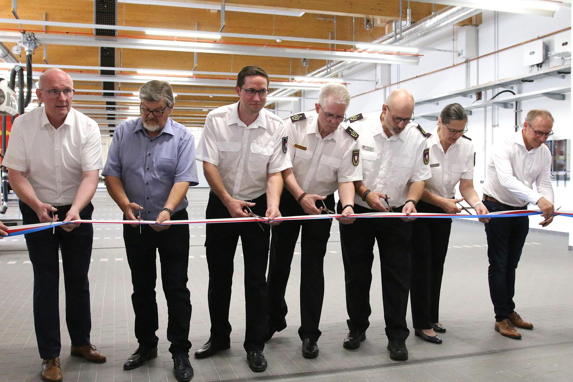 Landrat Jörg Farr, Planer Rolf Bruns, der Leiter der FTZ Jonas Ammerschubert, der ehemalige Kreisbrandmeister Klaus-Peter Grote, Kreisbrandmeister Joachim Muth, Kreisjugendfeuerwehrwartin Silke Weibels und Planer Uwe Brinkmann durchschneiden das Band zur Einweihung des Gebäudes.  (Foto: bb)