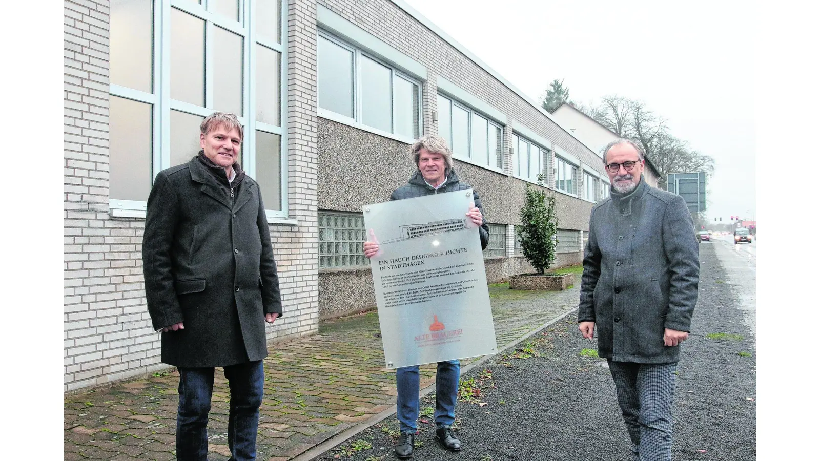 Friedrich-Wilhelm Lambrecht (Mitte) bringt gemeinsam mit Bürgermeister Oliver Theiß (li.) und Wirtschaftsförderer Lars Masurek das Schild an, das auf den baugeschichtlichen Hintergrund des Flaschenlagers im Gewerbepark „Alte Brauerei“ hinweist. (Foto: bb)