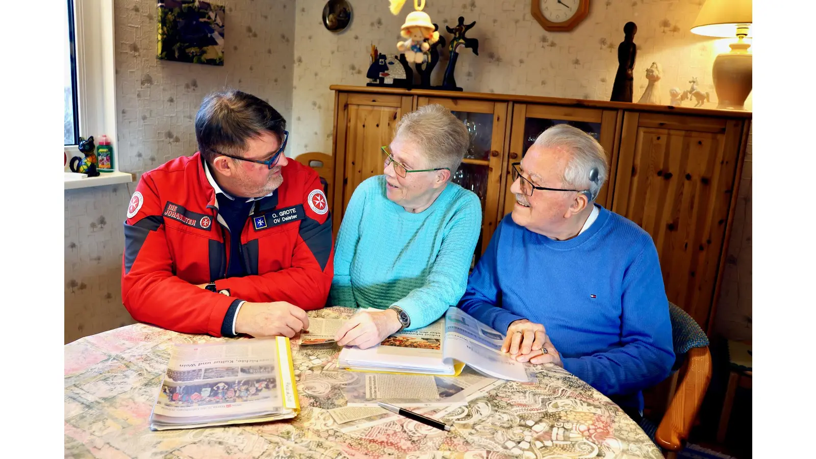 Olav Grote (rote Dienstjacke), Dienststellenleiter der Johanniter im Ortsverband Deister (Ronnenberg) im Gespräch mit langjährigen Kunden des Hausnotruf-Einsatzdienstes (Ehepaar Renate und Hans Mentner).  (Foto: Johanniter-Unfall-Hilfe e.V.)
